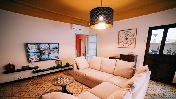 A living room with a beige sofa, a patterned rug, a television, and a decorative wall piece. - Casa Rural en el Centro Hist Rico de Gualta (Gualta)