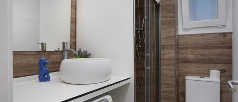 A modern bathroom with a white sink, a glass shower enclosure, a toilet, and a washing machine.