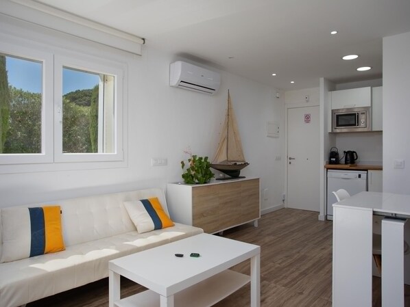 A modern, well-lit room with a white sofa, a small white table, a wooden cabinet, and a sailboat decoration.