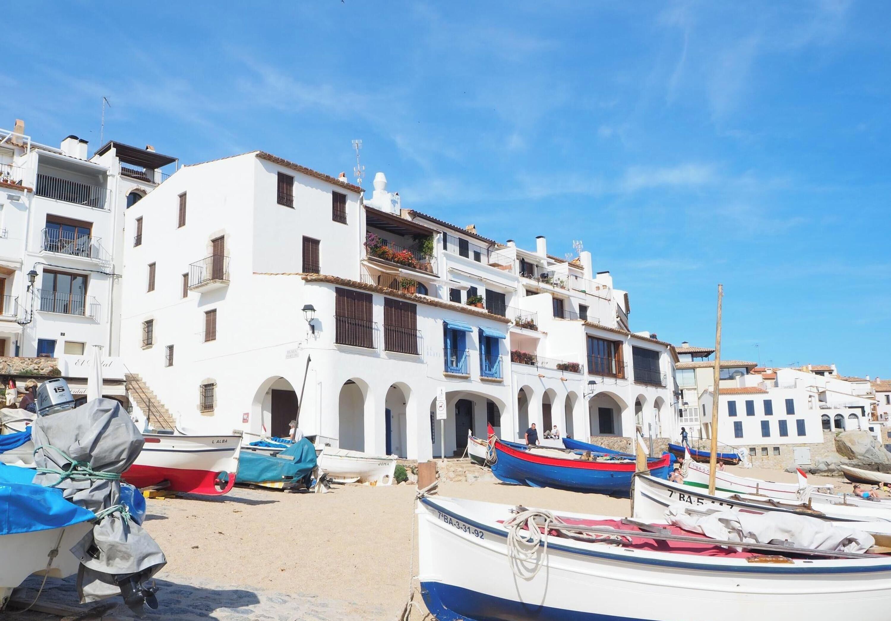 A coastal town with white buildings, a sandy beach, and several boats.