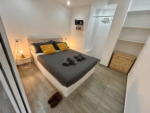 Un dormitorio moderno con cama, mesita de noche y cómoda de madera pequeña.