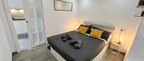 A modern bedroom with a bed, bedside table, and a mirror on the wall.