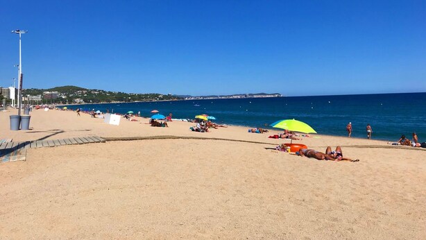 Une plage où l’on peut voir des gens se prélasser au soleil et nager, des parasols et un ciel bleu dégagé.