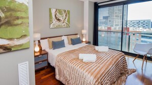 A modern hotel room with a large bed, a view of the city through the window, and a painting on the wall. - Victoria Diagonal Mar 2 Design Duplex Penthouse (Barcelona)