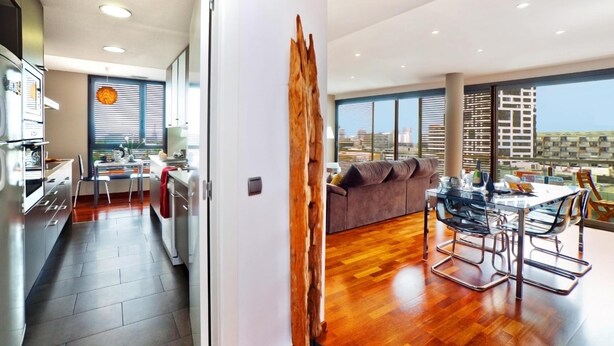 A modern living space with a kitchen, dining area, and a large window offering a city view. - Victoria Diagonal Mar 2 Design Duplex Penthouse (Barcelona)