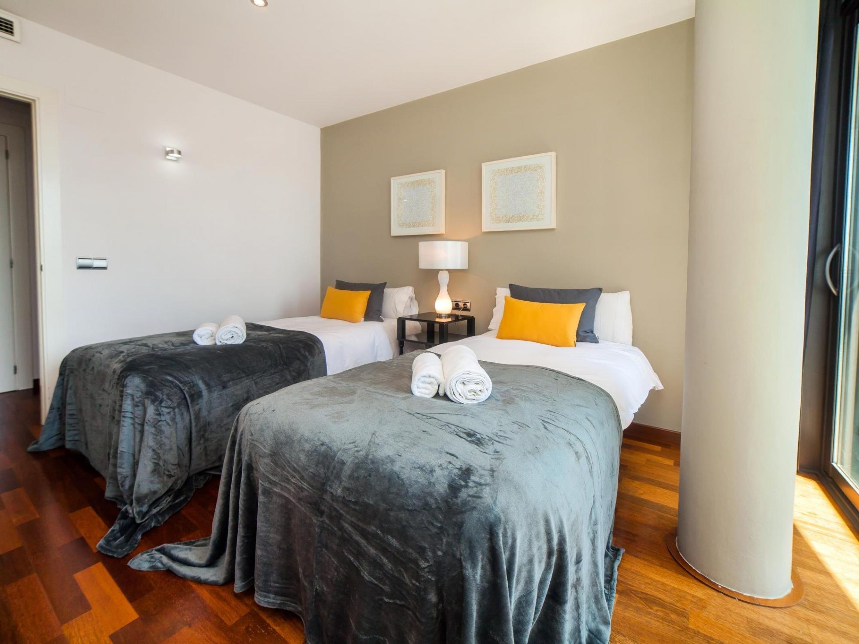 A hotel room with two beds, a nightstand, a lamp, and artwork on the wall.