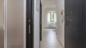 Um corredor com uma porta de madeira escura, uma parede branca e uma janela com cortinas brancas.