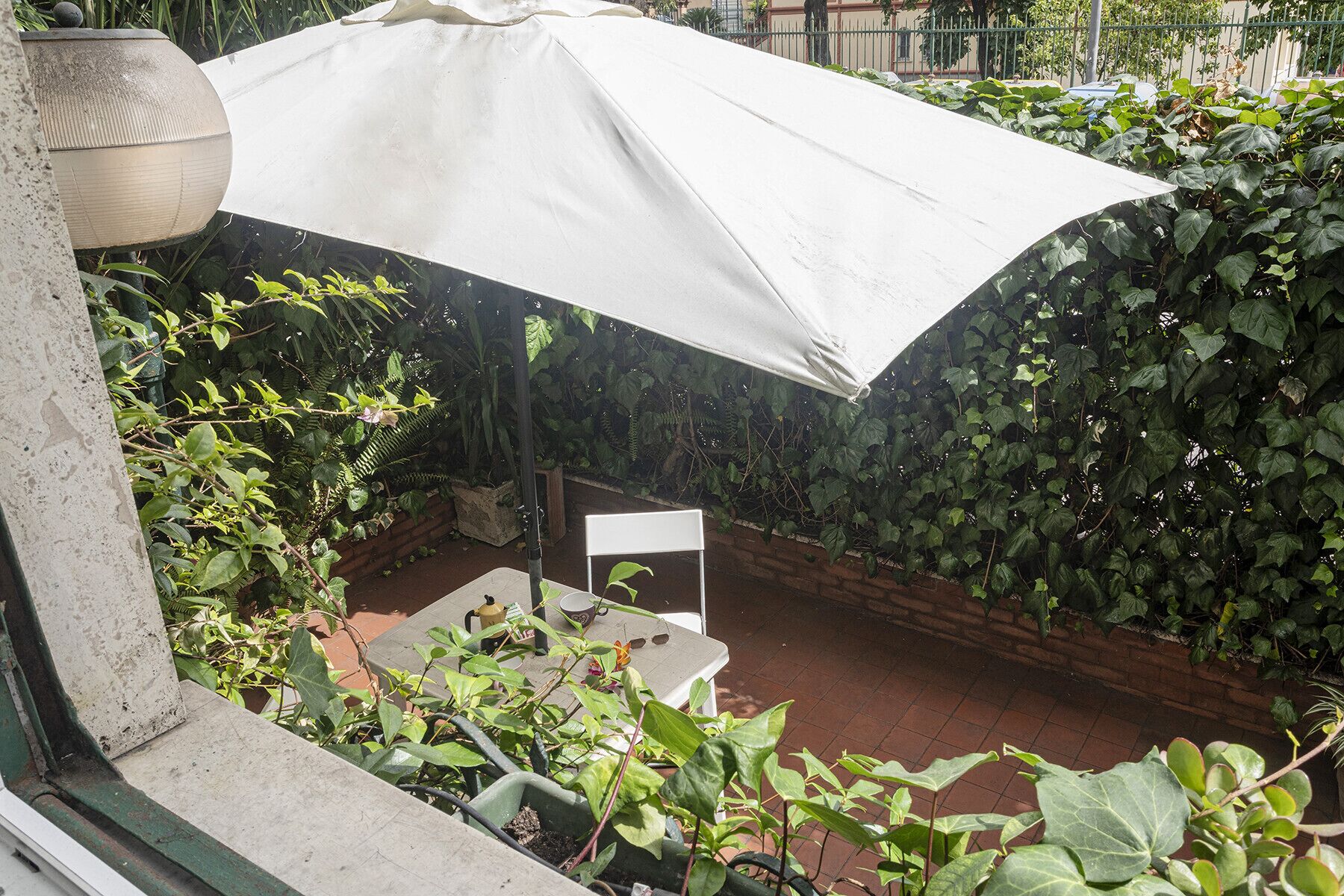 An outdoor patio with a covered seating area, surrounded by dense foliage and a brick wall.