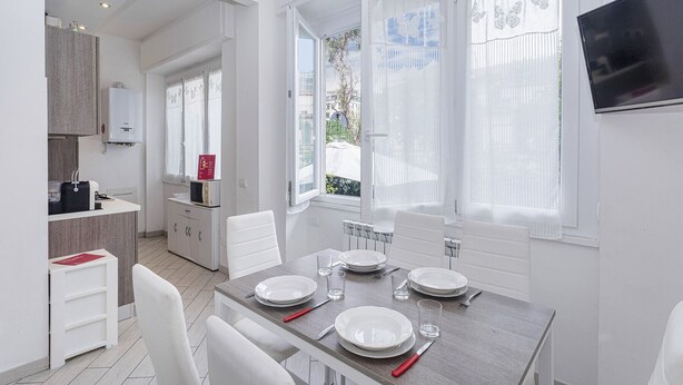 Uma cozinha moderna com armários brancos, micro-ondas e pia. Há uma área de jantar com mesa posta para quatro pessoas, incluindo pratos, copos e talheres.
