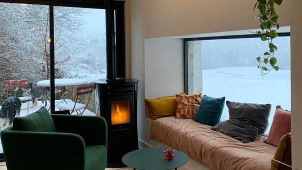 Un salon chaleureux avec une cheminée, de grandes fenêtres et une vue sur un paysage enneigé.