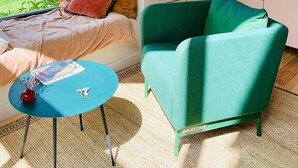 Un salon moderne doté d’une grande fenêtre, d’un fauteuil vert, d’une petite table ronde et d’un coin cuisine avec un évier et un plan de travail.