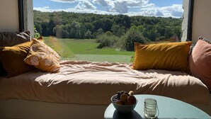 Un lit donnant sur une forêt et le ciel, vu à travers une fenêtre.