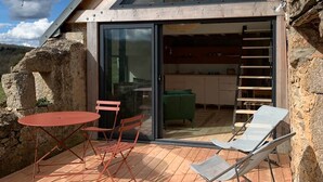 Une maison moderne dotée d’une terrasse en bois, d’une porte vitrée donnant sur la cuisine et d’un mur en pierre.