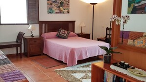 Een slaapkamer met een bed, nachtkastjes, een bureau, een stoel, een boekenkast, een raam en kunst aan de wanden.