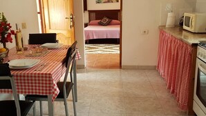 Een compacte keuken met een eethoek, een bed en uitzicht op een strand door een open deur.