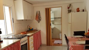 Een kleine keuken met een fornuis, oven en wastafel. Er is een eethoek met een tafel gedekt voor twee personen.