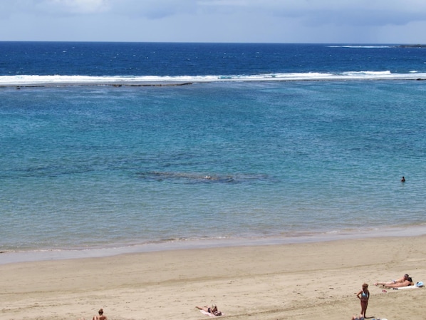 Ein Strand mit klarem, blauem Wasser, sandigem Ufer und Menschen, die sich sonnen.