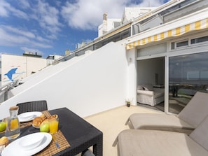 Ein Balkon mit Esstisch für das Frühstück, einer Couch und einer Glastür zu einem Innenraum.
