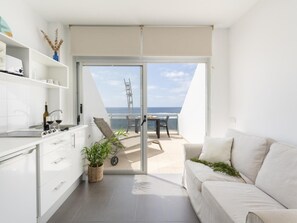 A modern kitchen with white cabinets, a dining area with a table and chairs, and a balcony with a view of the sea. - Apartamento Mars n Las Canteras Vista mar 308 (Las Palmas de Gran Canaria)