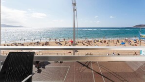 A beach with a metal sculpture, a paved area with chairs, and a clear view of the sea.