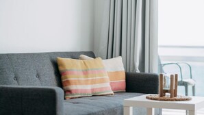 A grey sofa with striped pillows, a small white table with a woven coaster, and a round mirror on the wall.