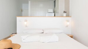 A neatly made bed with white linens, a straw hat, and sunglasses on the bedside table.