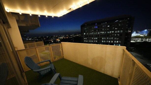 A balcony with two blue chairs, a string of lights, and a view of a cityscape at night. - Travel Professionals Downtown (Nashville)