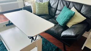 A room with a white foldable table, a black leather sofa with three cushions, and a green rug. - Travel Professionals Downtown (Nashville)
