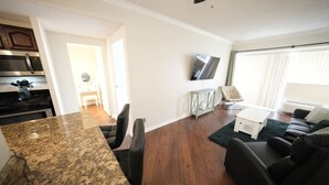A modern living room with a kitchen area, a flat-screen TV mounted on the wall, and a dining area with a granite countertop and chairs. - Travel Professionals Downtown (Nashville)