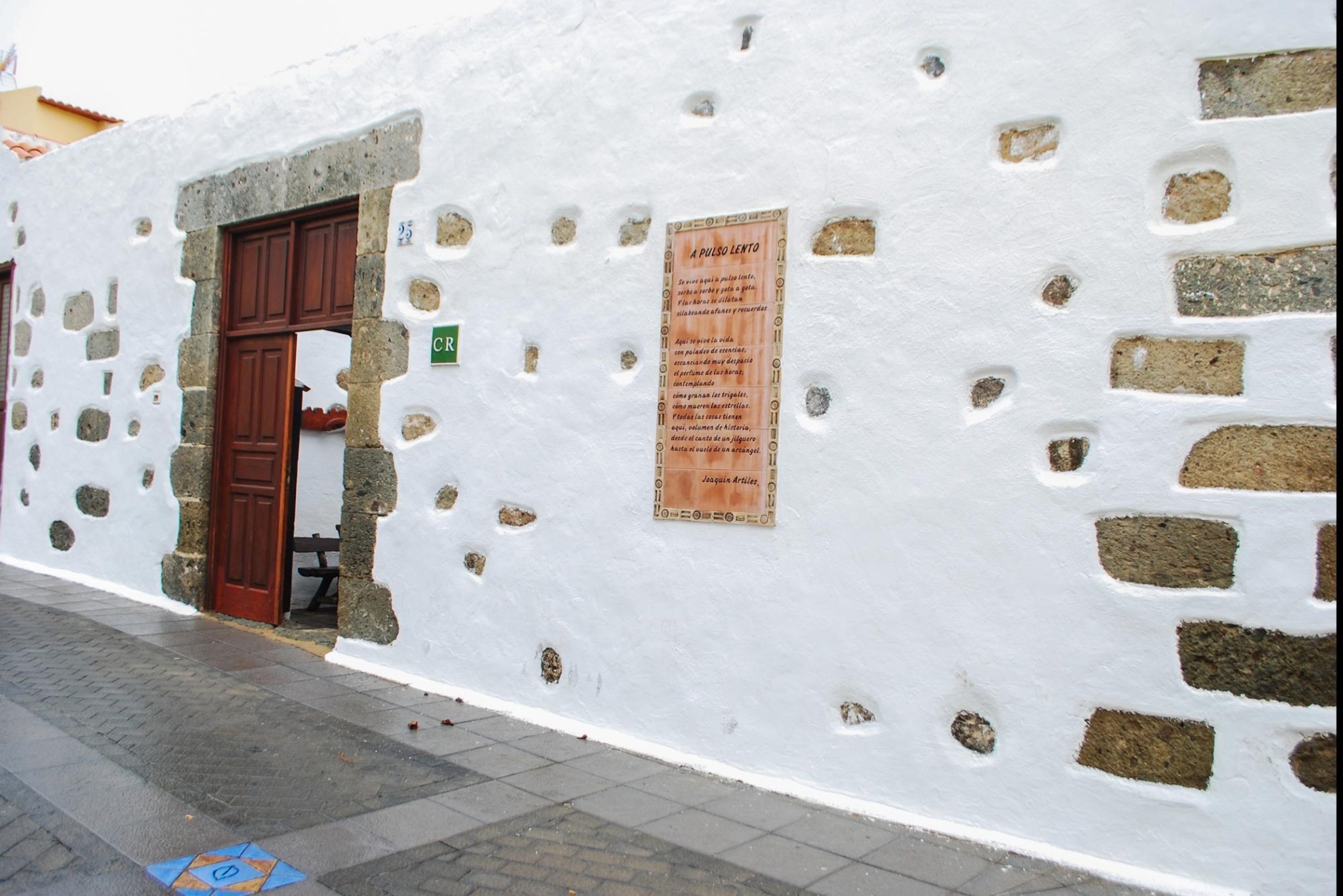 A white building with a stone facade, a wooden door, and a sign on the wall.