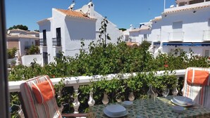 A terrace with a table set for dining, surrounded by white buildings and greenery.