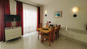 A dining area with a table, chairs, a television on a cabinet, and a window with curtains.