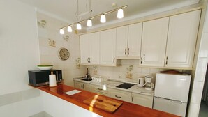 A modern kitchen with white cabinets, a wooden countertop, a microwave, a coffee maker, and a refrigerator.