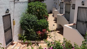 A narrow courtyard with white walls, black gates, and potted plants.