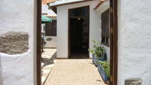 Une entrée étroite menant à un bâtiment doté d’une terrasse carrelée, d’un cadre de porte en bois et, au fond, d’un parapluie vert.