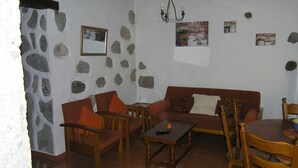 Un salon chaleureux avec un mur en pierre, un canapé marron, des chaises en bois, une table basse et un lustre.