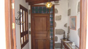 Une porte en bois ornée d’un vitrail, un mur de pierre et une petite table sur laquelle sont posés une lampe et un lampion.