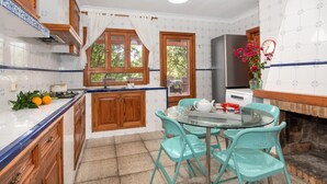 A kitchen with wooden cabinets, a gas stove, a sink, a window with curtains, a refrigerator, and a table with chairs. - Sa Volta Nova Beautiful House in Countryside (Porreres)