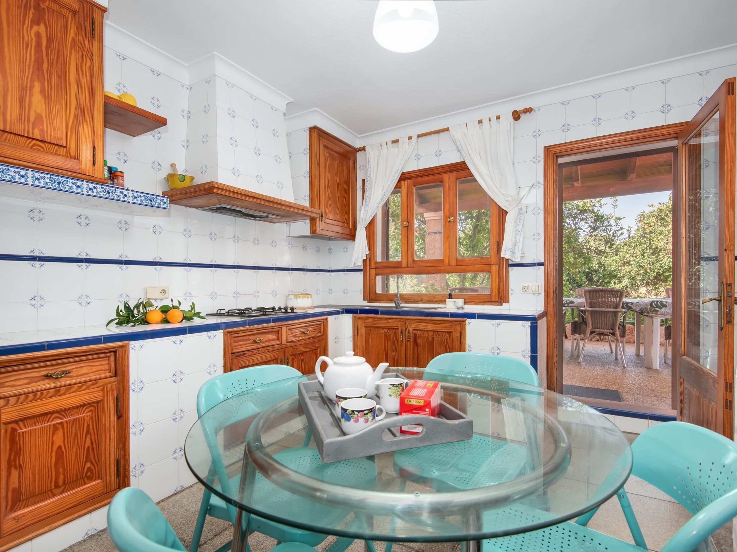 Una cucina con mobili in legno, un tavolo in vetro e vista su uno spazio esterno attraverso una porta vetrata.