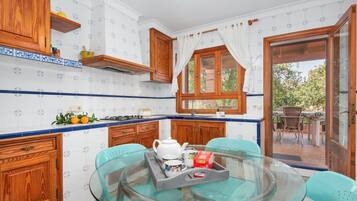 Una cucina con mobili in legno, un tavolo in vetro e vista su uno spazio esterno attraverso una porta vetrata.