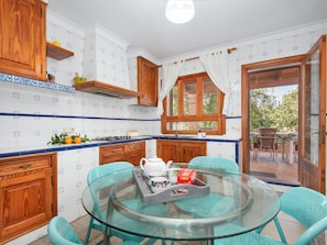 A kitchen with wooden cabinets, a glass table, and a view through a glass door to an outdoor area. - Sa Volta Nova Beautiful House in Countryside (Porreres)