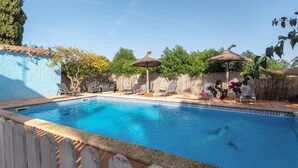 A swimming pool with a tiled edge, surrounded by lounge chairs and umbrellas, with a wooden fence and greenery in the background. - Sa Volta Nova Beautiful House in Countryside (Porreres)