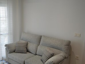 A grey sofa with patterned cushions in a room with white walls and a window with sheer curtains. - Apartamento Delf n Torrecilla (Nerja)