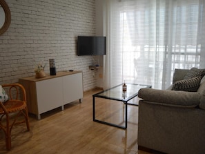 A living room with a brick wall, a flat-screen TV, a glass coffee table, a sofa, and a wicker chair. - Apartamento Delf n Torrecilla (Nerja)