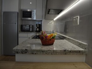 A kitchen with a granite countertop, a microwave, a coffee maker, and a basket of flowers. - Apartamento Delf n Torrecilla (Nerja)