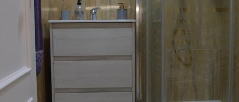 Un baño con cabina de ducha de vidrio, tocador blanco con espejo y una toalla morada en la pared.