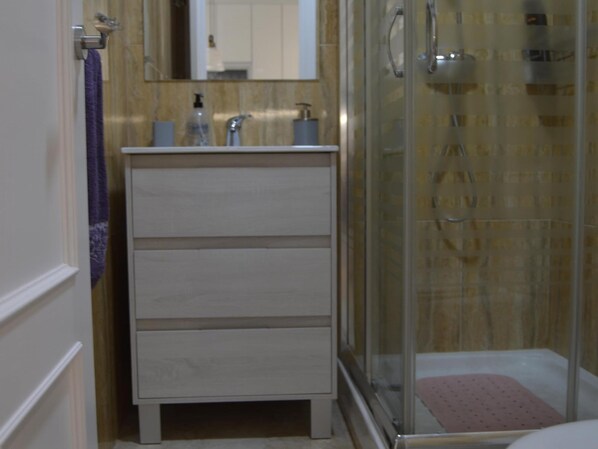 A bathroom with a glass shower enclosure, a white vanity with a mirror, and a purple towel on the wall.