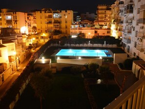 A swimming pool surrounded by buildings at night.