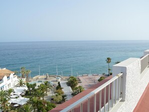 A coastal hotel with a view of the sea, palm trees, and a promenade with umbrellas.