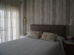 A neatly made bed with floral pillows, a wooden headboard, and a bedside table with a lamp. - Apartamento Delf n Torrecilla (Nerja)